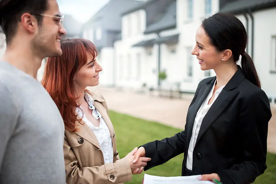 Eine Maklerin begrüßt Klienten vor einem Haus